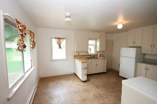 view of kitchen from interior doorway, view of sink, fridge, cupbords area to right of photo